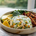 Close up of a bowl with a portion of chickpea rice in a bowl with slices of avocado and tempeh behind it.