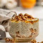 Close up of a jar layered with morir soñando chia pudding and orange crumble with an orange in the background.