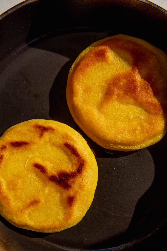 The arepas after cooking and flipping in a pan with nice char marks.