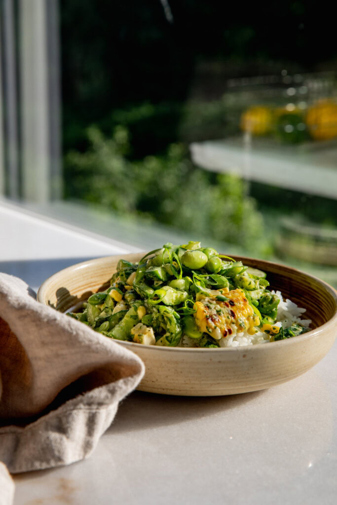 A bowl of corn cucumber salad in a bowl by a large window.