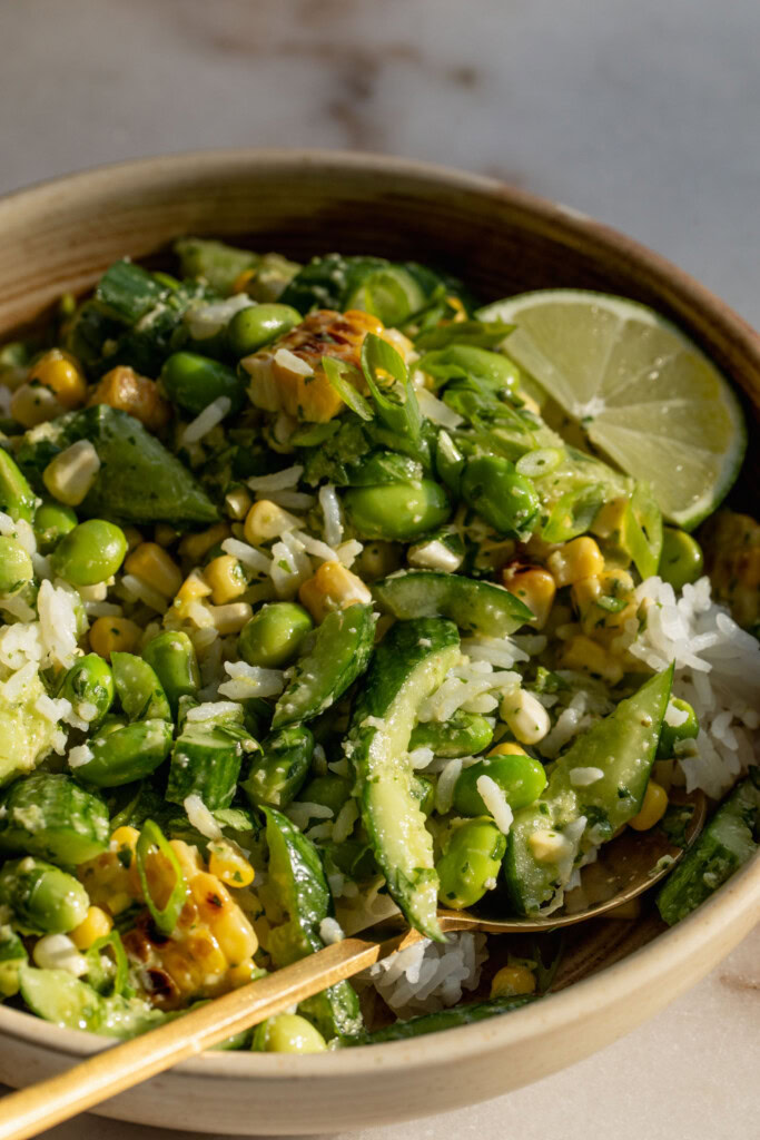 Serving bowl filled with rice mixed together with the corn cucumber salad with a wedge of lime tucked into the back.
