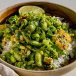 Bowl of grilled corn and smashed cucumber salad served over a bowl of rice with a wedge of lime.