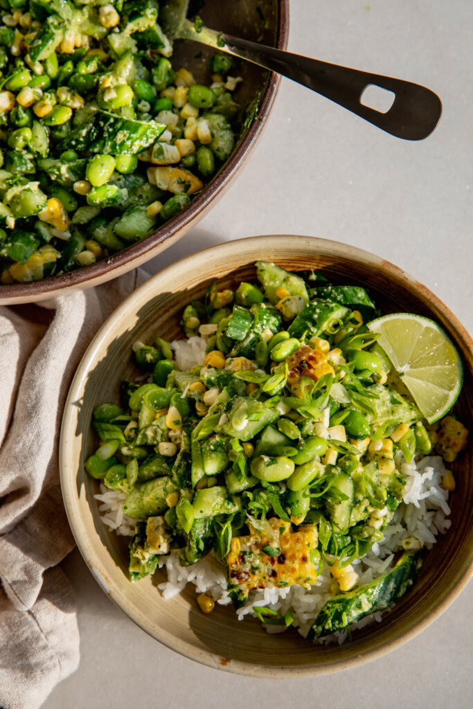 Bowl of edamame cucumber salad over rice next to a large mixing off to the side.