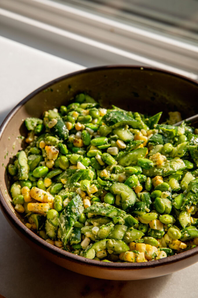 A large mixed bowl of grilled corn, edamame, and cucumber tossed in a scallion dressing.