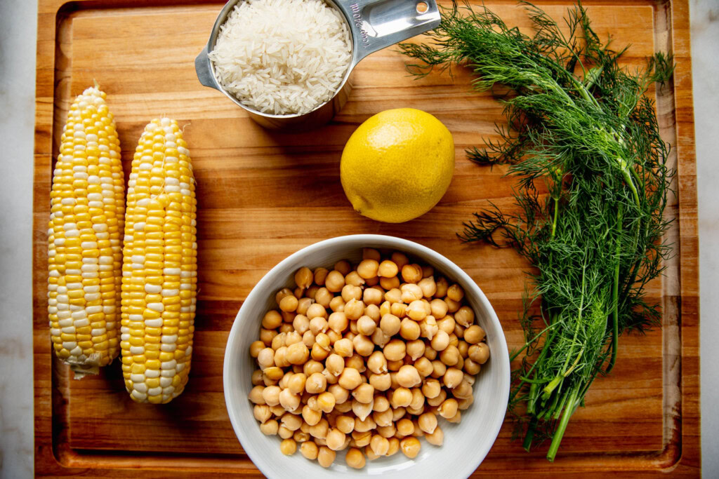 Cutting board with chickpeas, dill, rice, lemon, and corn.