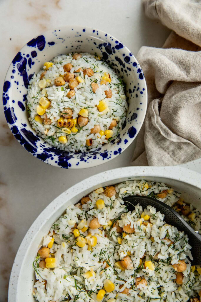 A portioned bowl of mixed rice next to the pot of rice, chickpeas, and corn.