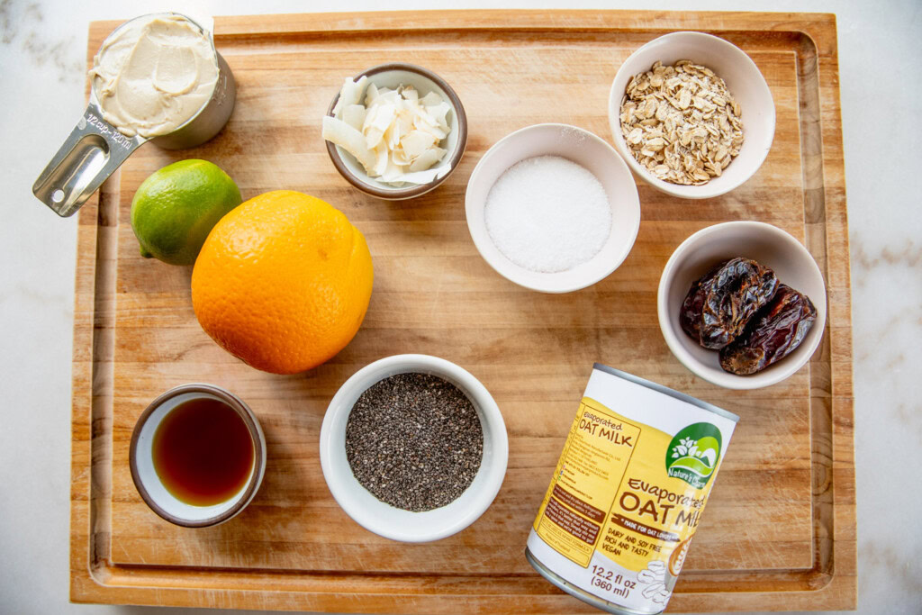 Cutting board topped with lime, orange, chia seeds, agave syrup, evaporated milk, dates, oats, coconut flakes, and yogurt.