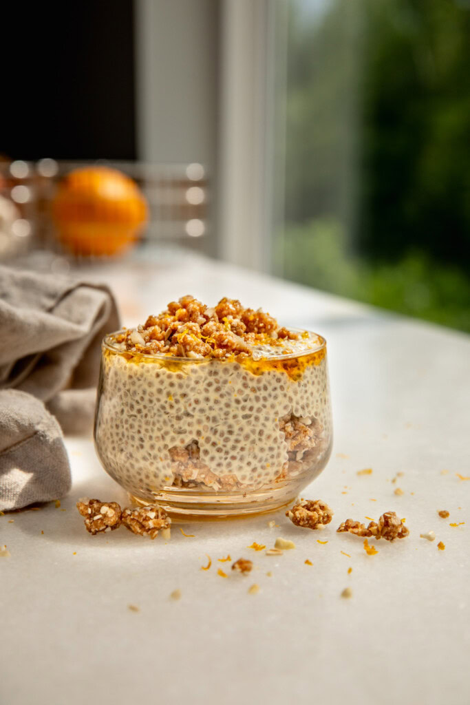 Close up of a cup of layered chia pudding and crumble hit with light from the window.