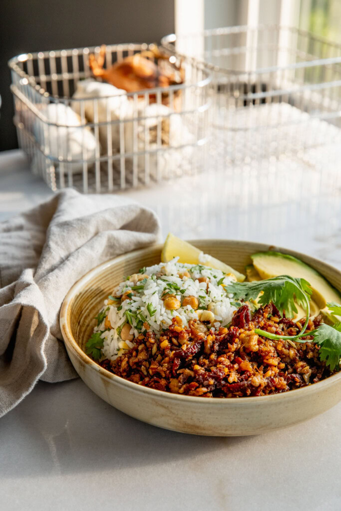 A bowl filled with a dome of rice, avocado slices, a wedge of lemon and sun-dried tomato tempeh.