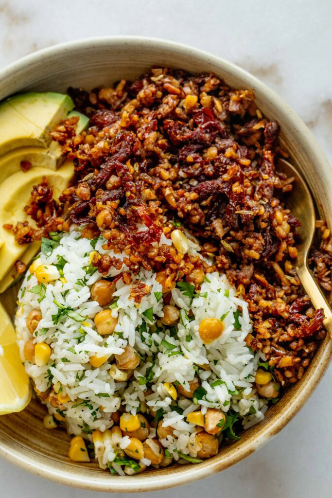 Bowl filled with high fiber rice, shredded tempeh, avocado, and a wedge of lemon.