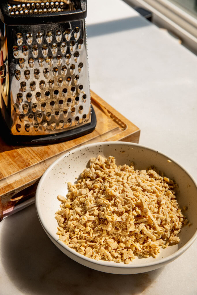 A bowl of shredded tempeh next to a box grater.