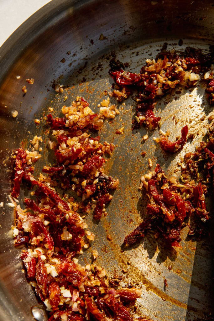 Mixing the onions, sun-dried tomatoes, and spices together in a pan.