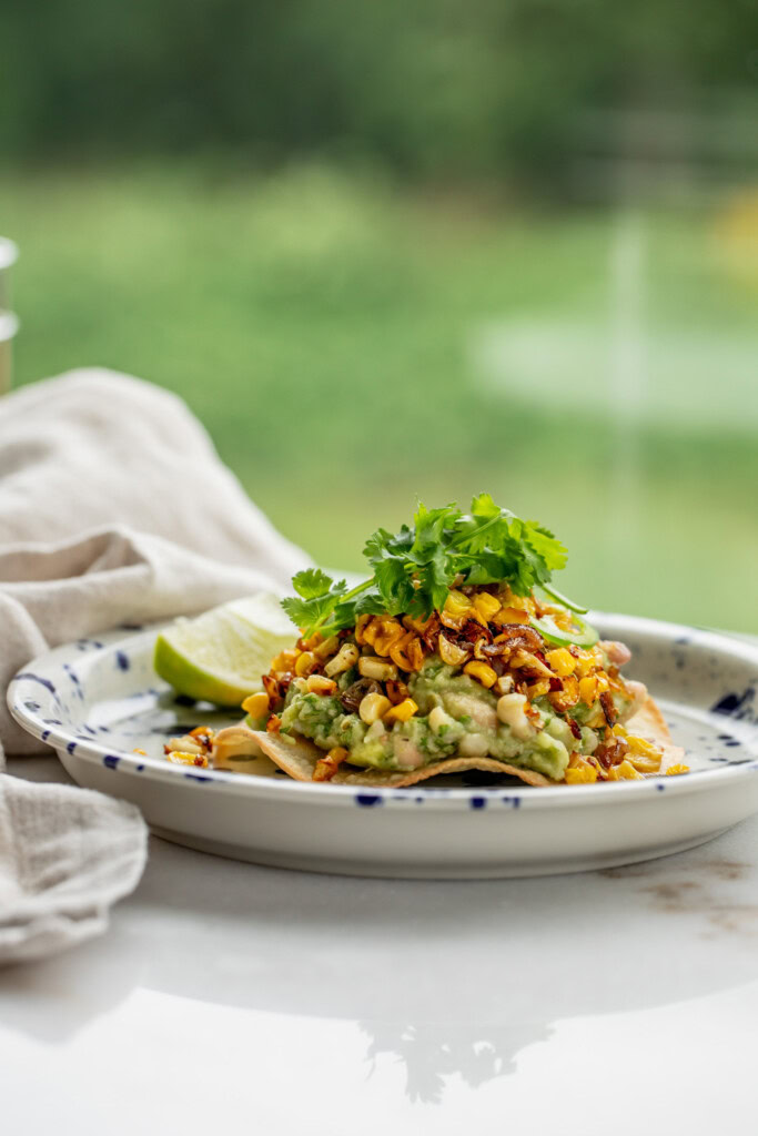 One tostada on a plate piled high with the avocado bean mash, crispy corn, and cilantro.