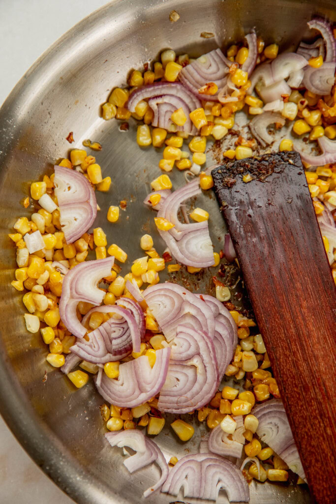 Toasted corn in a pan and shallots in a pan.