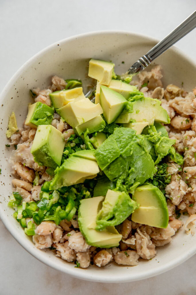 Adding the avocado, herbs, cilantro, jalapenos and brine together in a bowl.