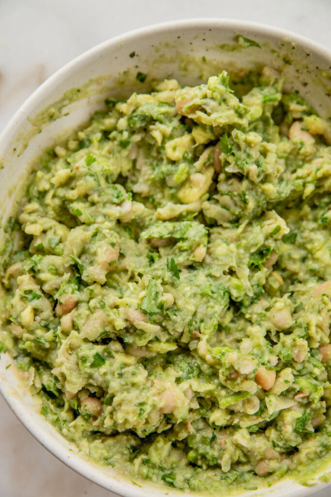 Mashing the avocado and beans together in a bowl with a fork.