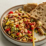 Plate of bean salad being scooped up with a spoon and bread tucked onto the side.
