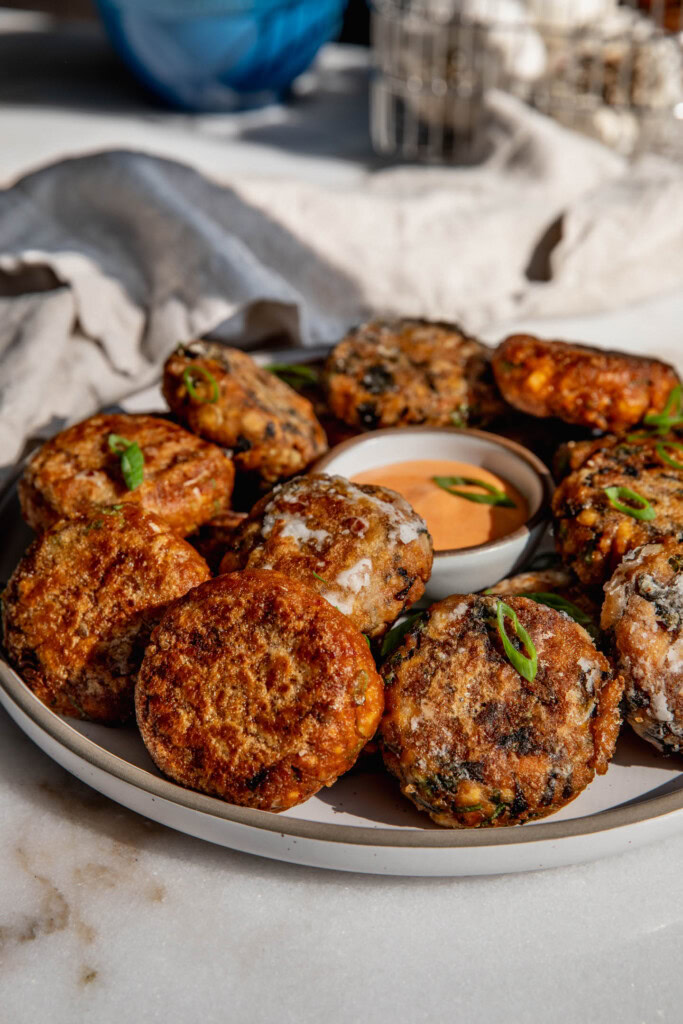 Close up of a plate with tofu patties piled around a bowl of dipping sauce.