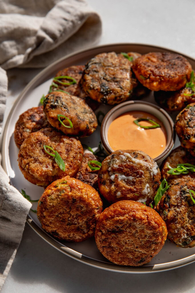 Plate of tofu patties in three different flavors with a bowl of dipping sauce tucked into the middle.