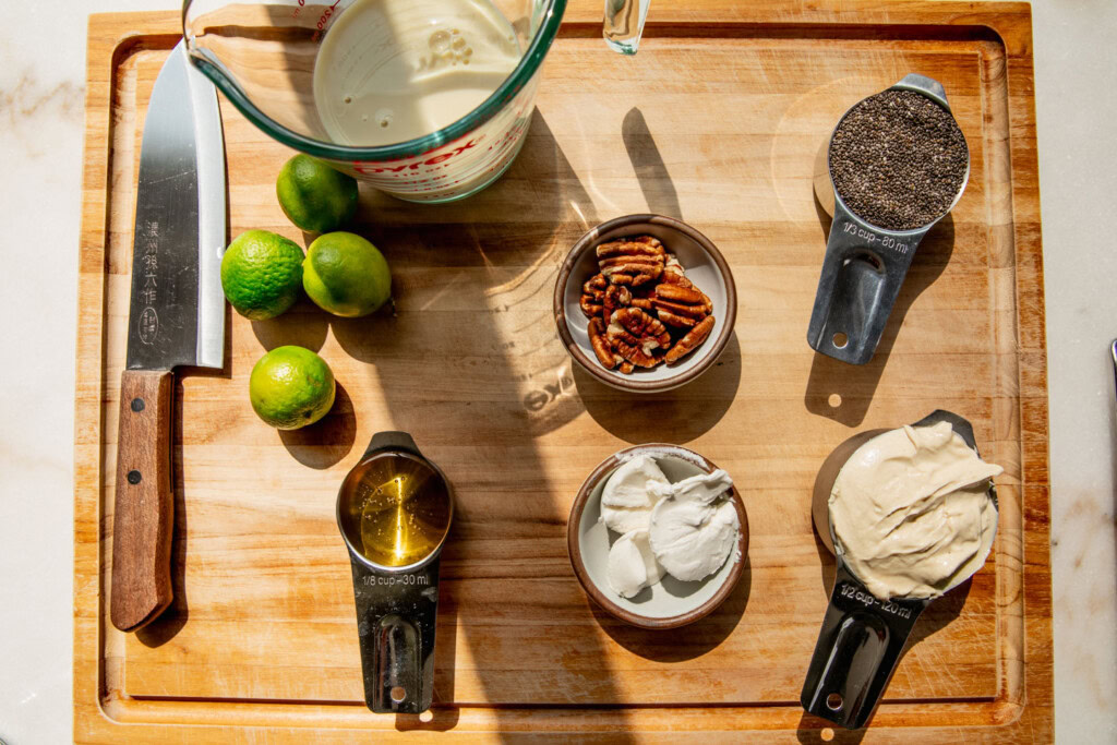 Cutting board topped with milk, yogurt, chia seeds, pecans, key limes and agave.