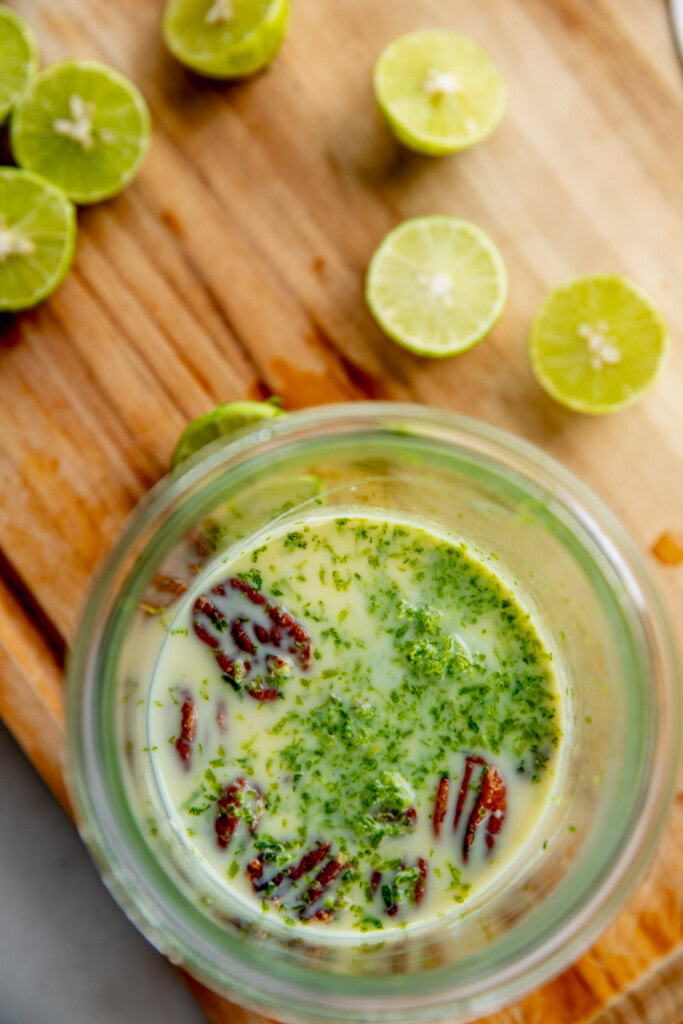 Key limes scattered over a cutting board with a jar filled with milk, yogurt, pecans, and key lime juice.