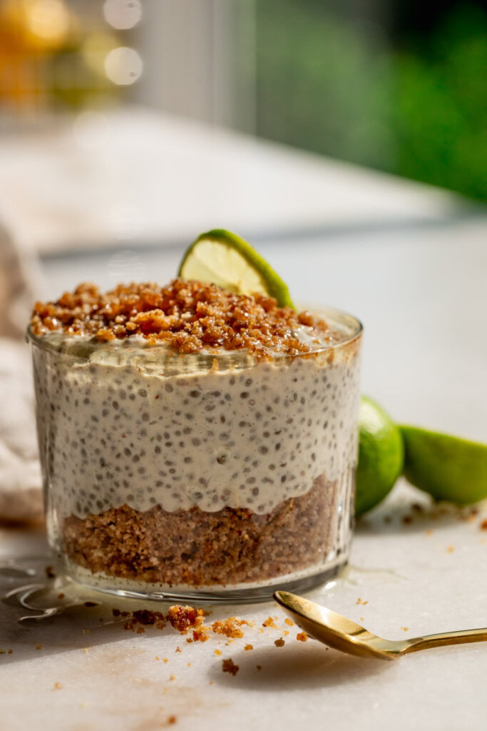 A jar of chia pudding layered with graham cracker crumb by the window with key limes set in the background.