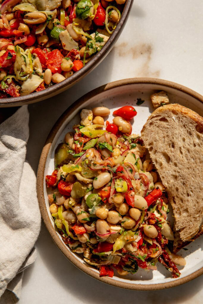 Bean salad piled onto a plate with a slice of bread tucked to the side.