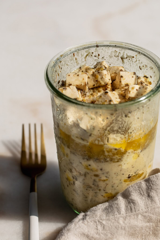 A glass container filled with tofu in a marinade with a fork set to the side.