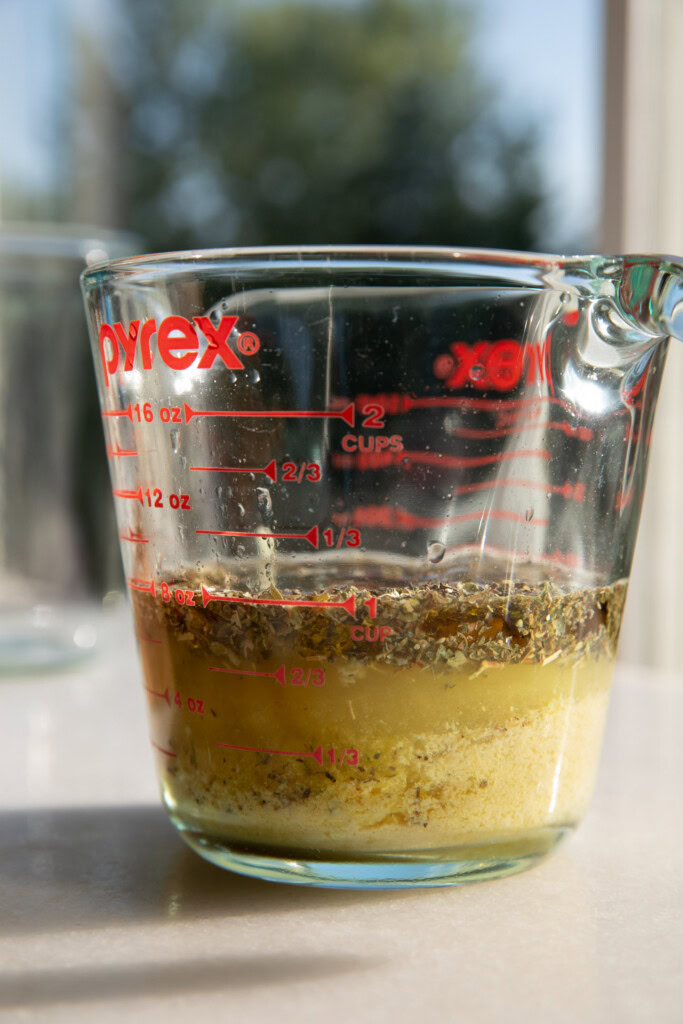 Oil, lemon, garlic, nutritional yeast, dry herbs, miso, and apple cider vinegar in a glass measuring cup.