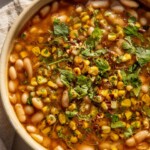 Bowl of corn simmered beans topped with corn and cilantro.
