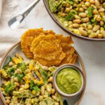Plate of charred corn bean salad tossed in a zucchini salsa served with tostones and a small bowl of extra salsa. Serving dish is in the top corner from the plate.