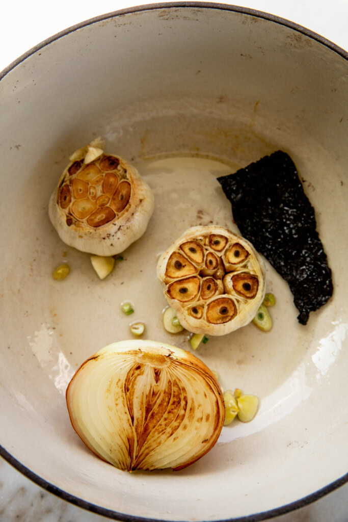 Caramelized garlic bulbs, onion, and chili in a pot.