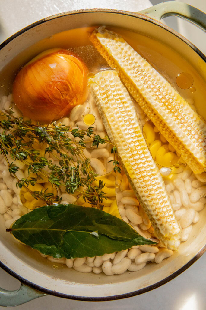 Beans in a pot with water, corn cobs, onion, thymes, bay leaf and oil.