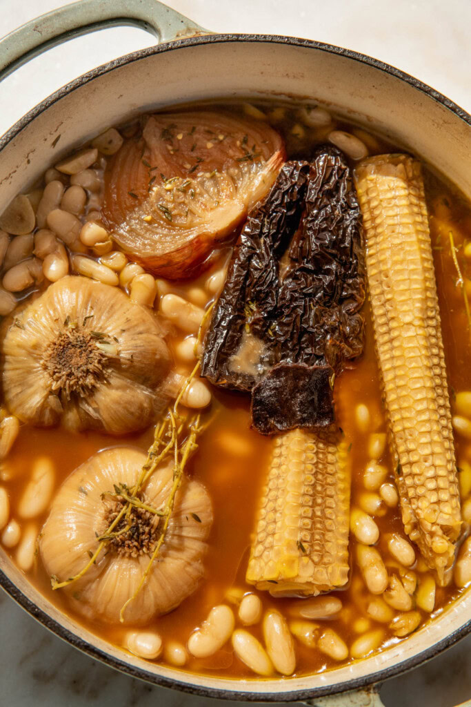 Beans simmered away in a pot with corn cobs, onion, garlic bulbs, chilies, and thyme.