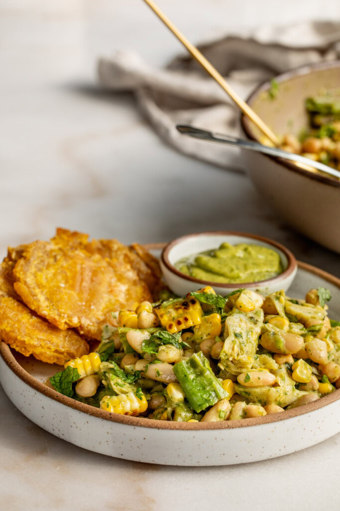 Side view of a plate of salsa beans served with plantains and extra zucchini salsa.