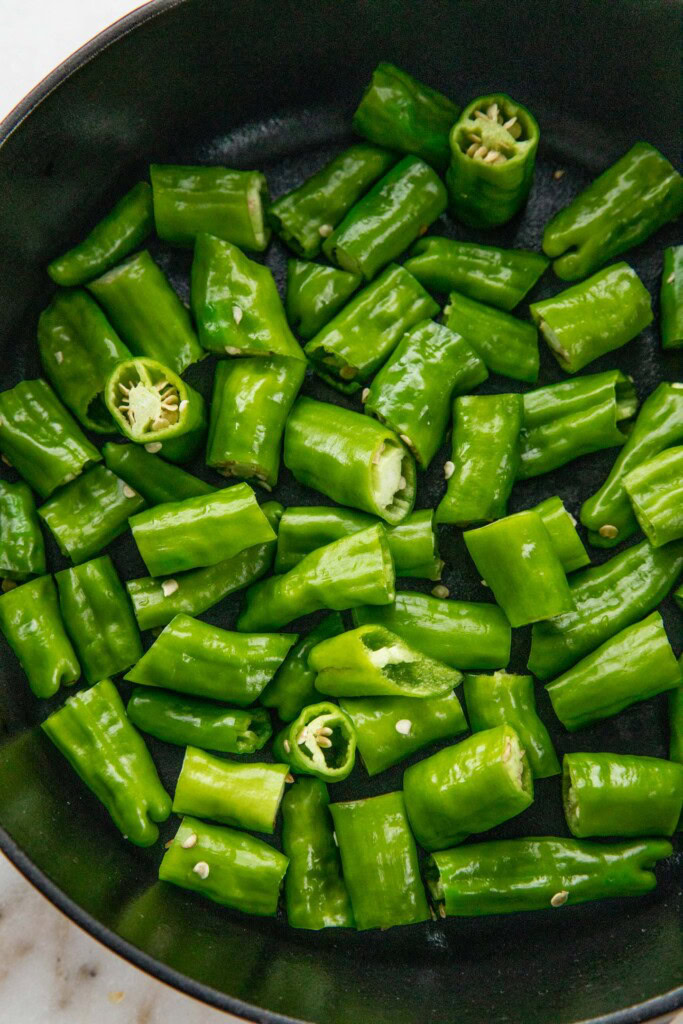 Shishito peppers in a dry cast-iron pan.