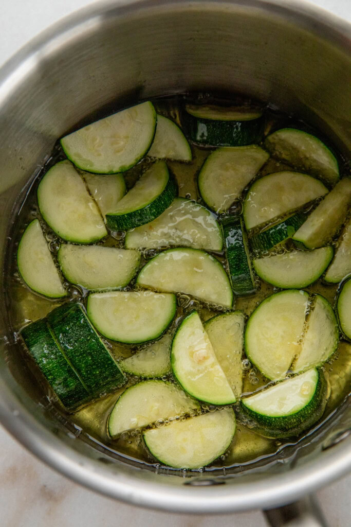 Zucchini cooking in oil in a pan.