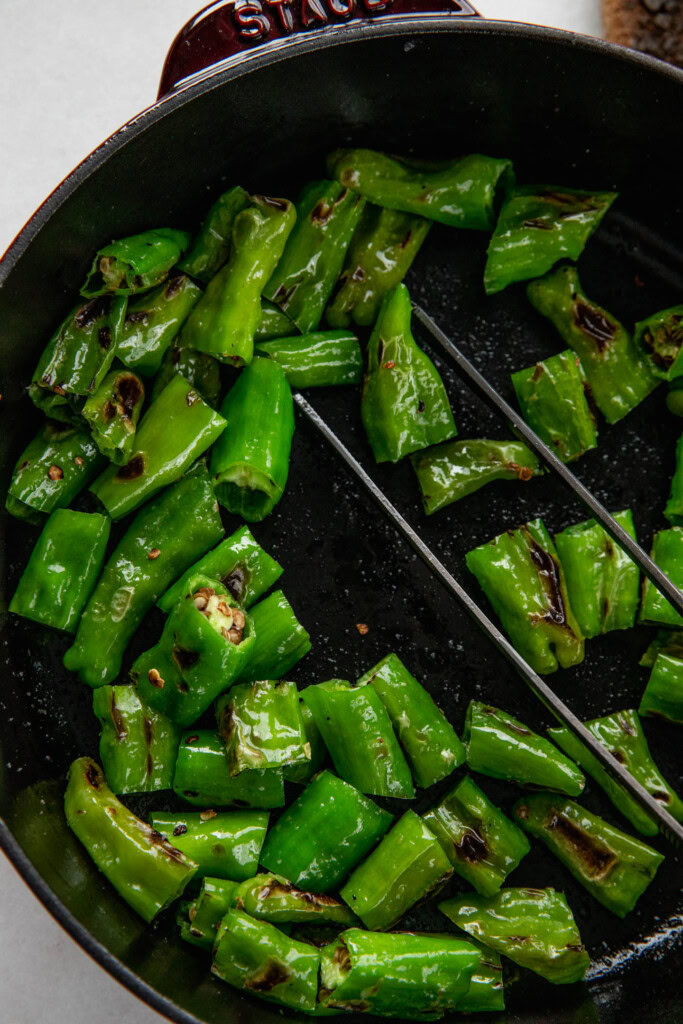 Charred shishito peppers in a cast-iron pan.