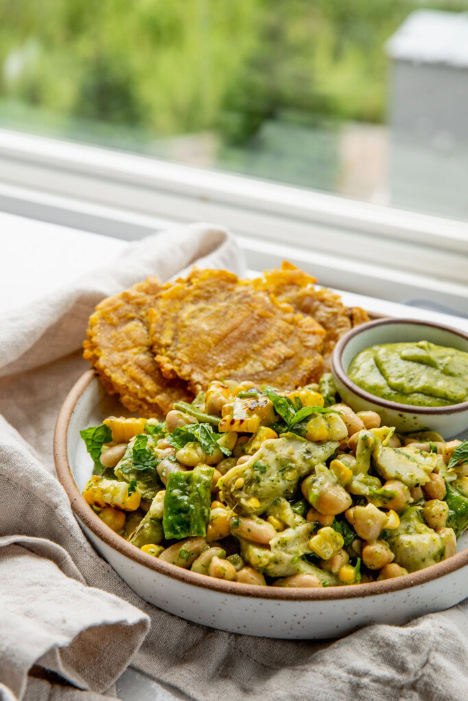Salsa beans served on a plate alongside tostones and a small bowl of zucchini salsa for dipping.