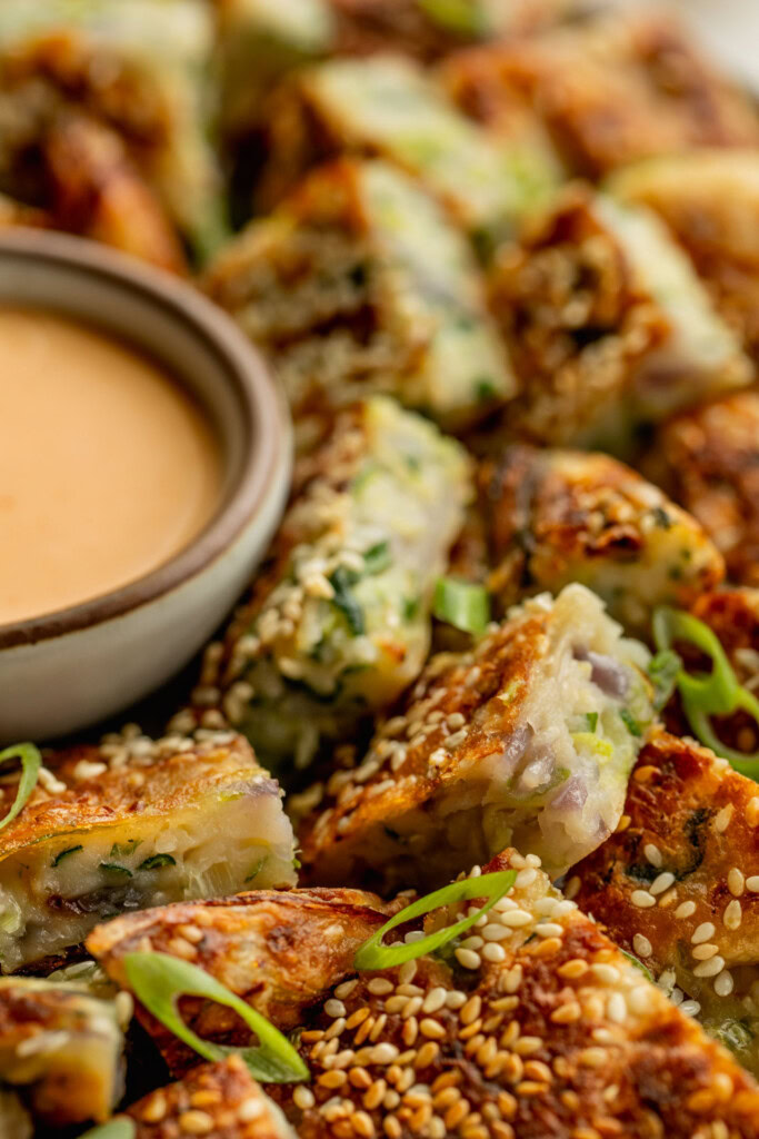 Close up of zucchini bites arranged on a plate with a bowl of dip to the side.