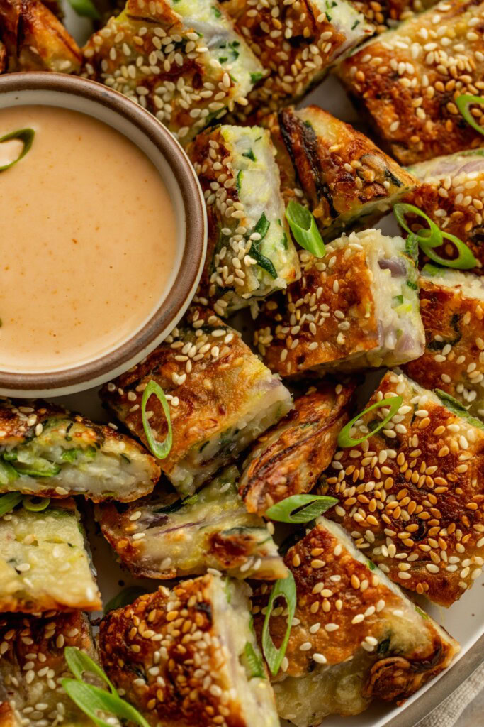 Close up of some cut up zucchini pancakes served with a bowl of dip.