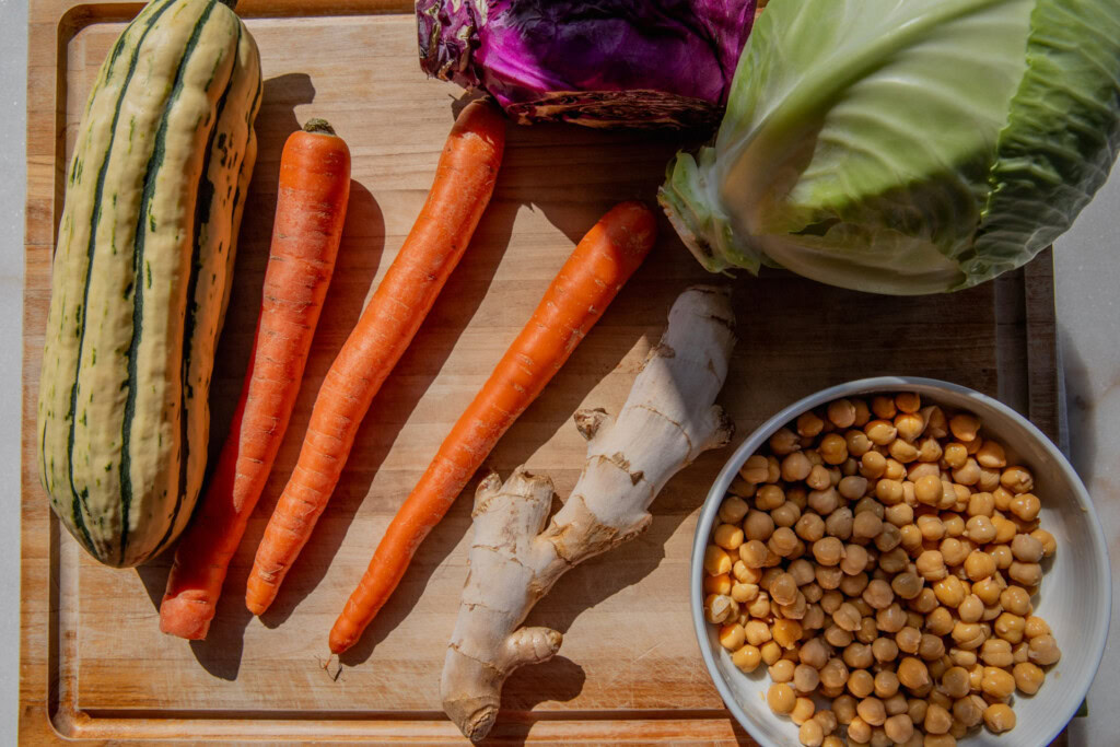 Cutting board with cabbage, carrots, delicata squash, a bowl of chickpeas and ginger.