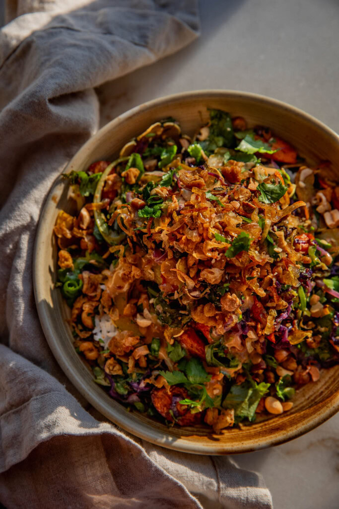 Top down view of a bowl filled with rice, the roasted carrot salad, chickpeas, fried shallots and peanut hoisin sauce.