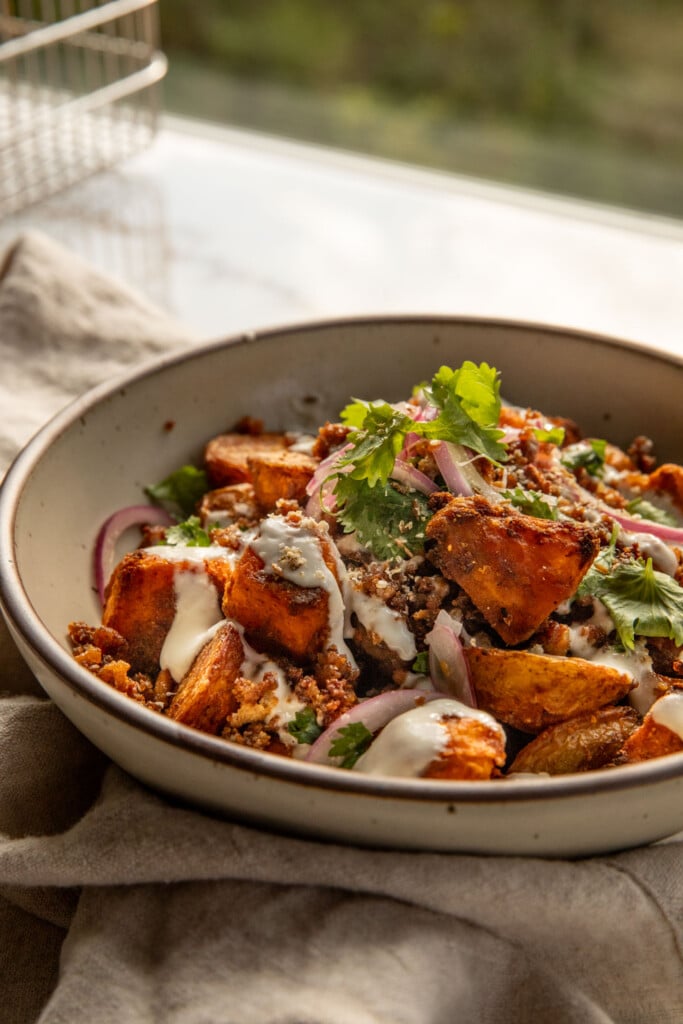 Bowl of potatoes and crumbled tofu piled high with marinated onions.